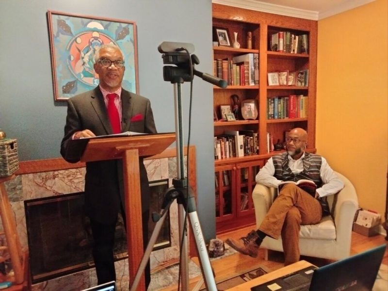 Left: Rev. Duncan Teague speaks at the podium. Right: Craig Washington, seated with an open book in his lap. looks on.